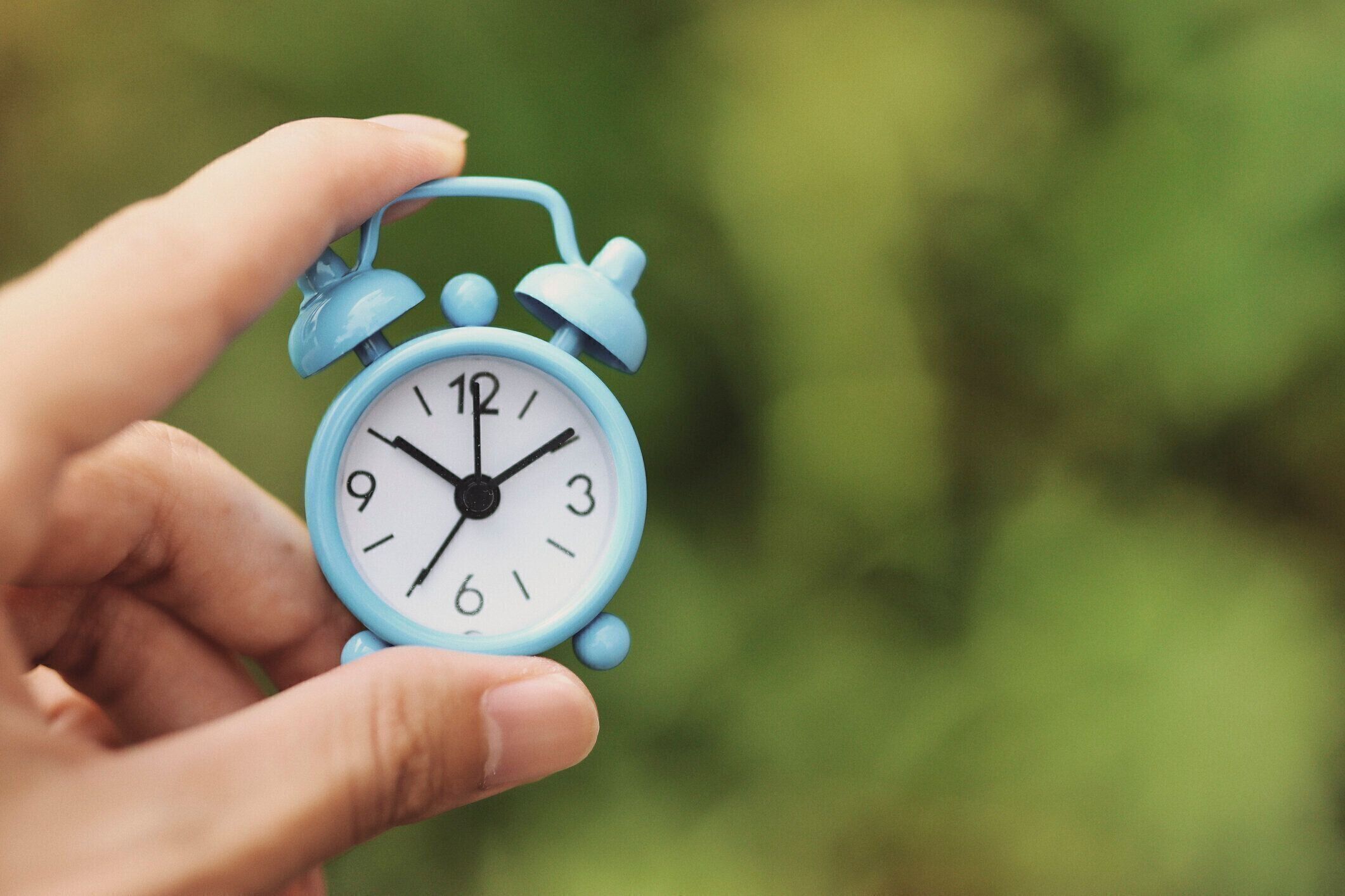 水色の目覚まし時計と人間の手