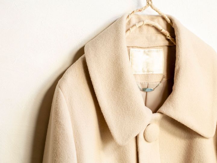 白い背景に服のハンガーにぶら下がるベージュのウールのコート