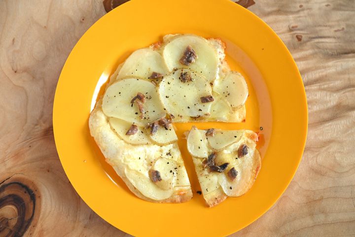 黄色の皿にのったじゃがいもとアンチョビのピザ