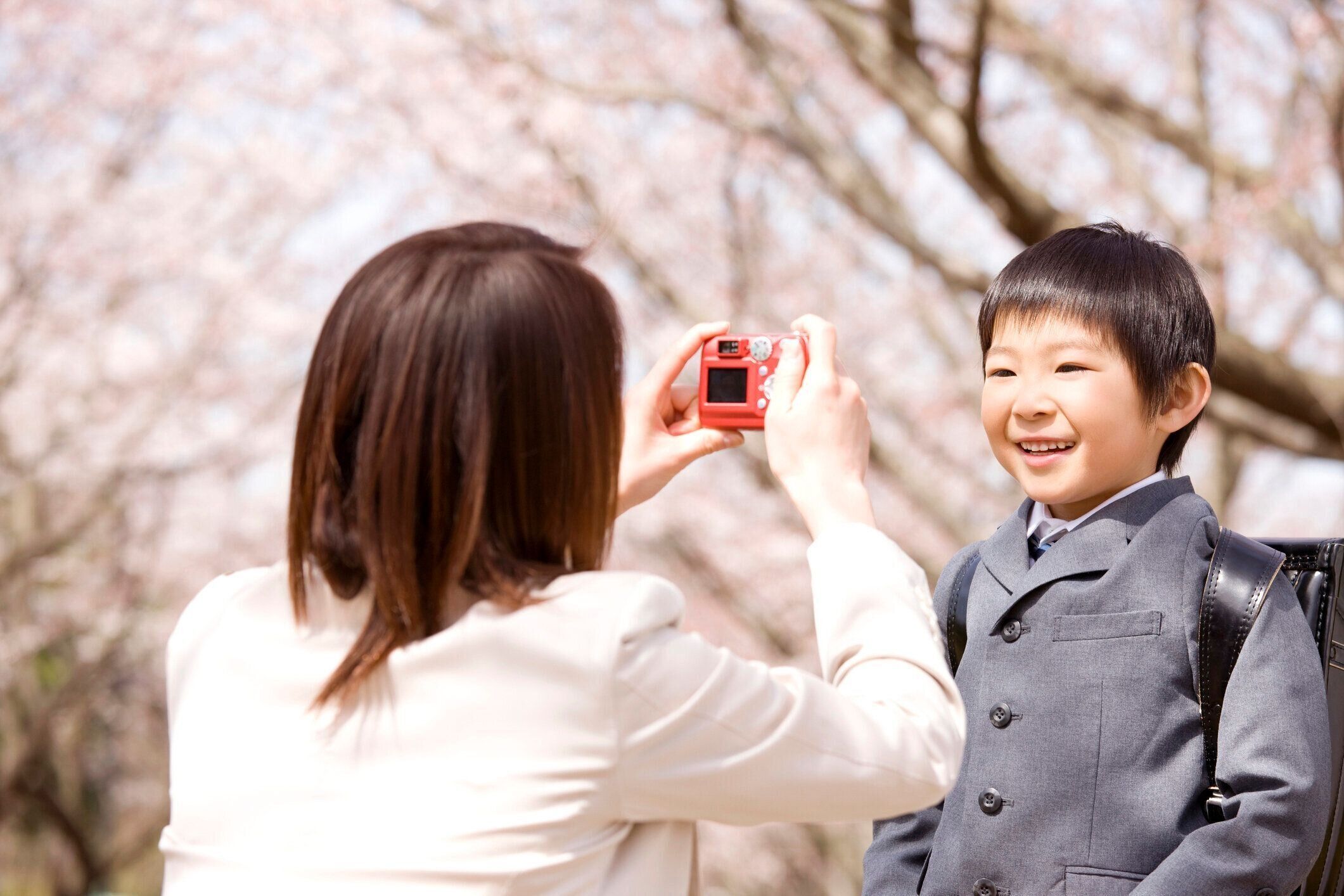 母は桜の木の下で彼の息子の写真を撮る