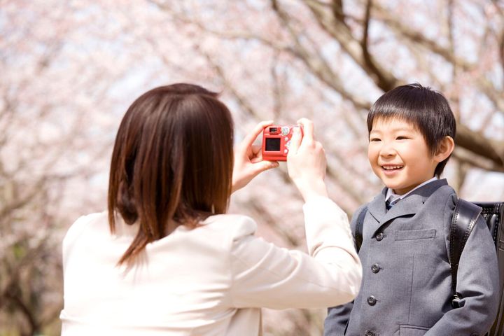 母は桜の木の下で彼の息子の写真を撮る