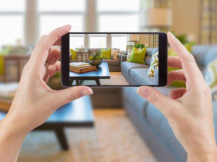 女性両手スマート電話の背後にある家インテリア リビング ルームの写真を表示します。