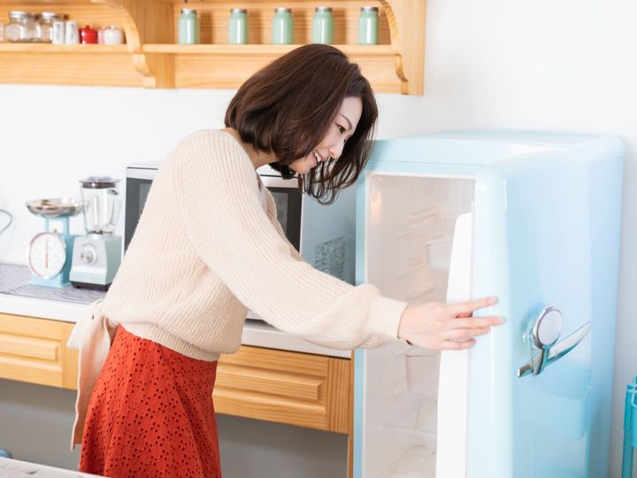 キッチン、冷蔵庫で魅力的なアジアの女性料理