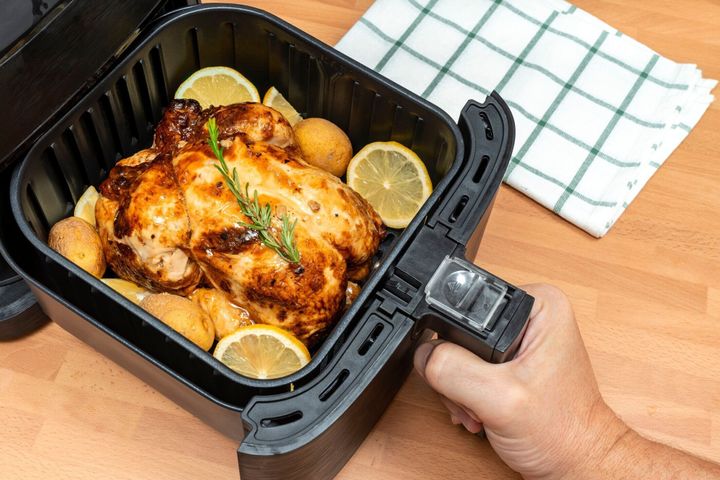 キッチンでエアフライヤーに付け合わせを施したローストチキン全体を手で調理します。平面図。