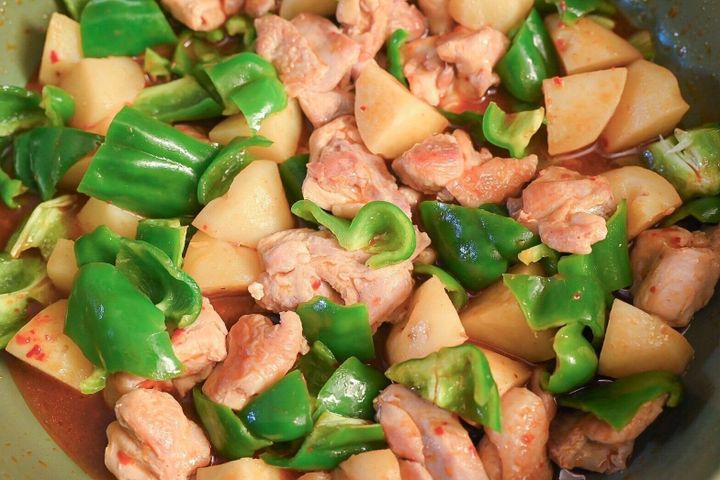 フライパンに入った炒めた鶏もも肉、じゃがいも、ピーマン