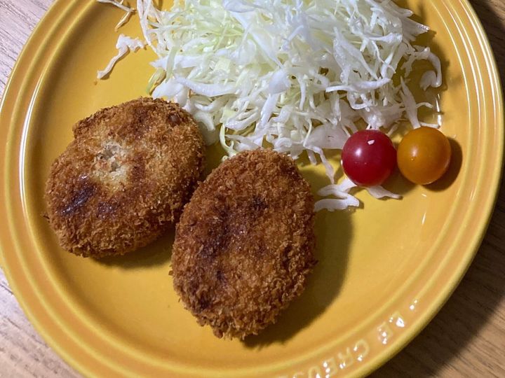お皿に盛られているメンチカツとキャベツとミニトマト
