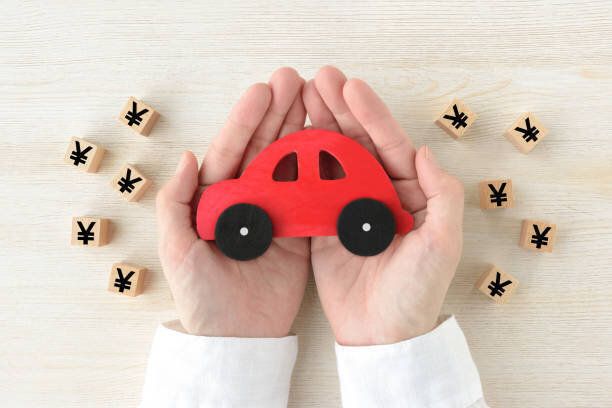 人間の手に囲まれた赤い車のおもちゃ木製のブロック、日本円のマーク