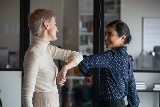 フレンドリーな笑顔ミレニアル世代の多様な女性の同僚は、社会的な距離を保ちます。