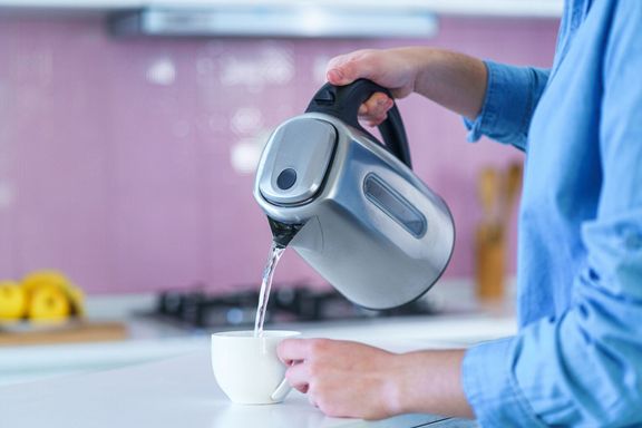 お茶を作るために電気ケトルからカップにお湯を注ぐ女性