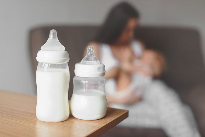 彼女の手と母乳、赤ちゃんを持つお母さんの背景に母乳ボトル。マタニティと赤ちゃんのケア。