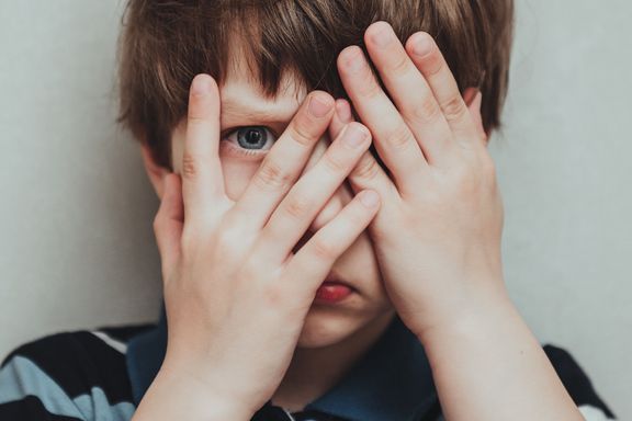 不幸な子供の男の子の手は彼の顔、子供のメンタルヘルスの概念、世界自閉症啓発日、十代の自閉症スペクトラム障害意識コンセプトを隠します