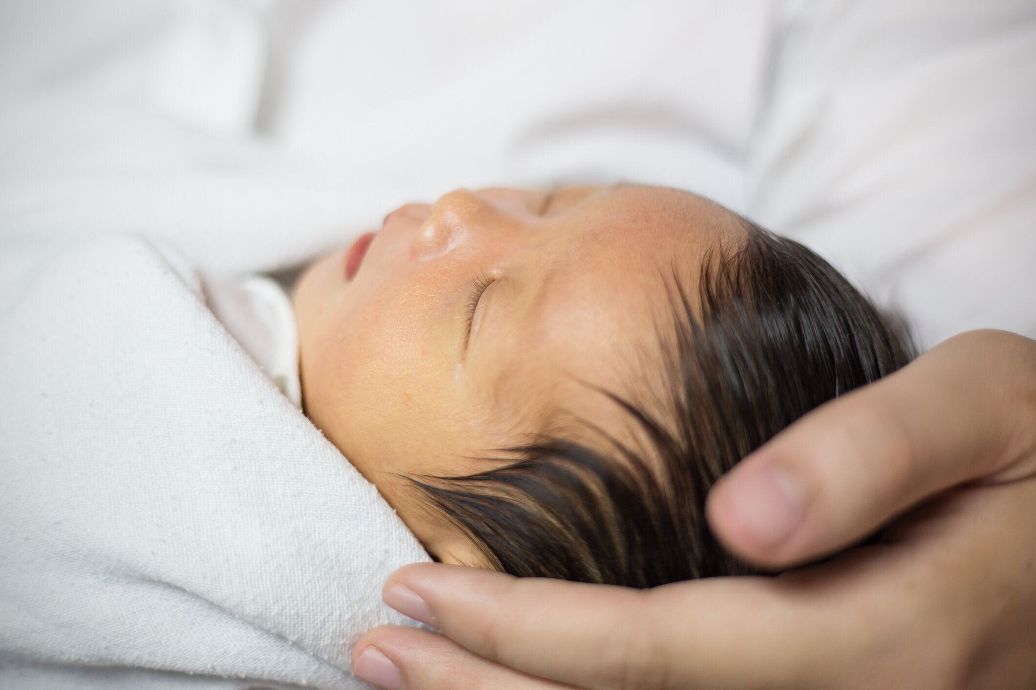 親手保持ヘッドで眠っているアジア人の新生児のクローズアップポートレート