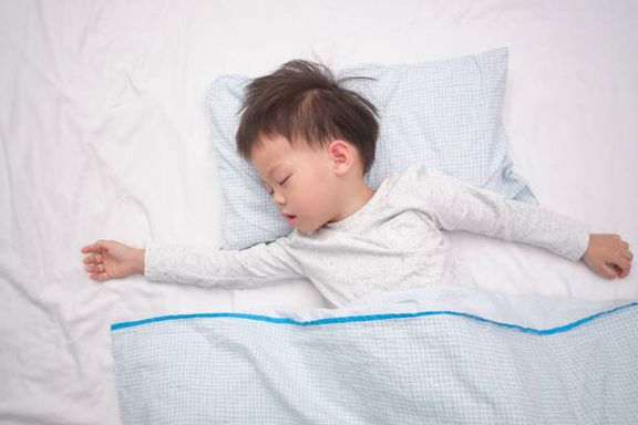 かわいいアジアの3 - 4歳の幼児の男の子は、ベッドで白いベッドのシートの上に背中に寝て、昼寝を取ってパジャマで子供