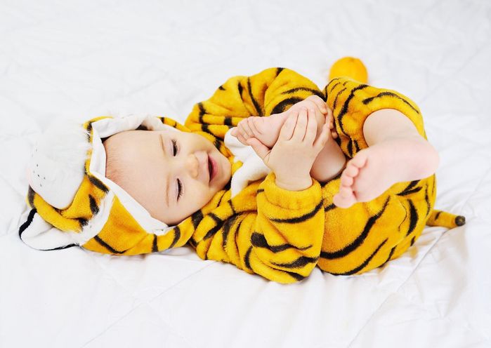 虎の衣装を着た赤ちゃんは白い背景に横たわって足を噛みます。虎の年