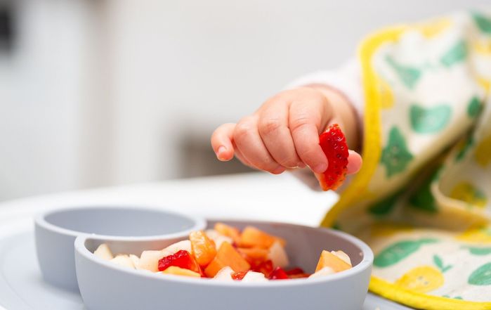 健康的な食べ物を食べる子供の椅子の子供に座っている果物の一部と赤ちゃんの手のマクロクローズアップ