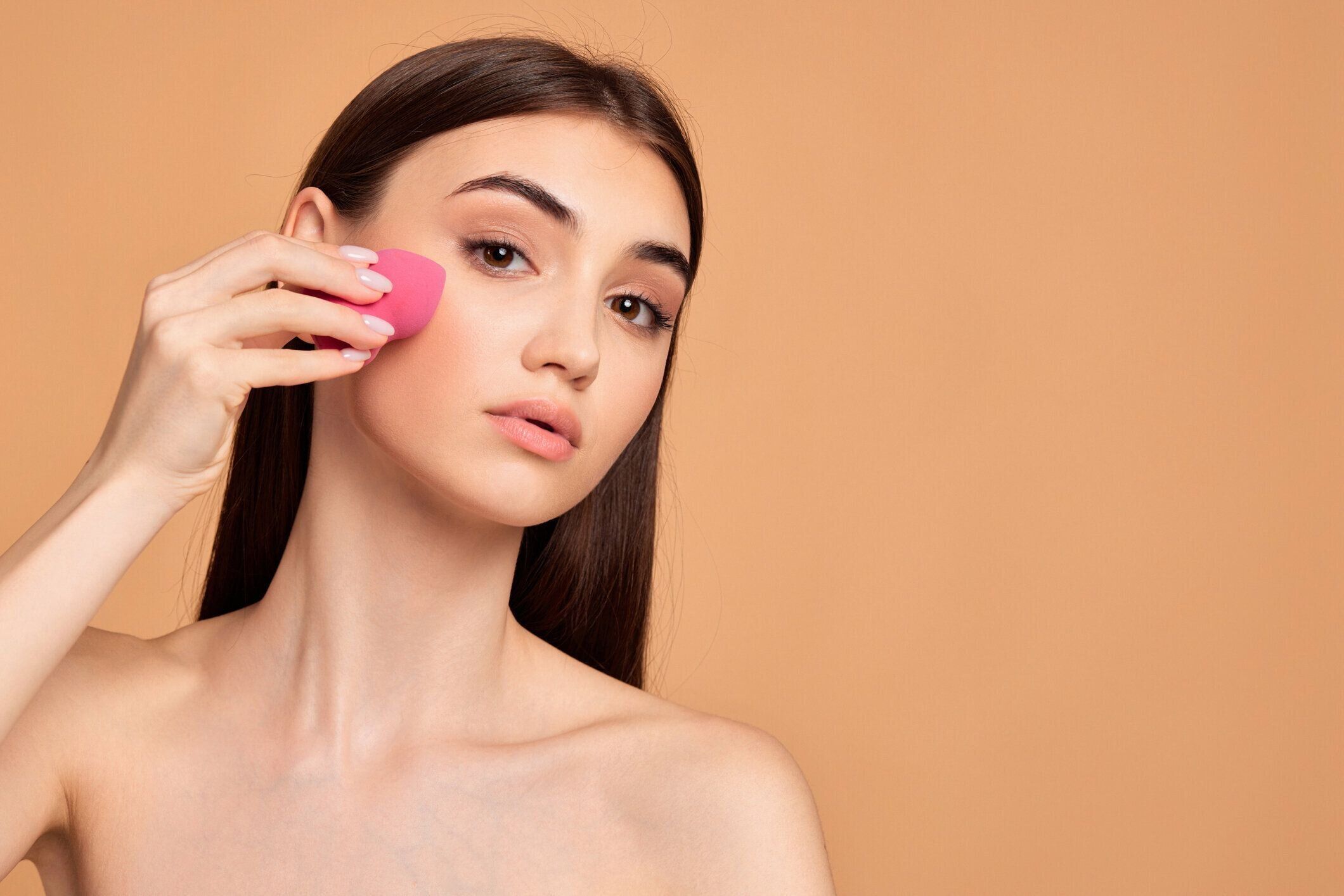 ピンクの化粧用スポンジでポーズをとる若い女性