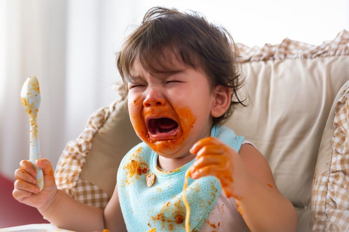 赤ちゃんの椅子に食べ物を食べ終わったときに満足していないときに泣いている愛らしい小さな幼児の女の子や幼児の赤ちゃん。かわいい幼児の女の子は空腹になり、より多くの食べ物をし�