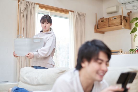 家事をしている妻とゲームをしているアジアの夫