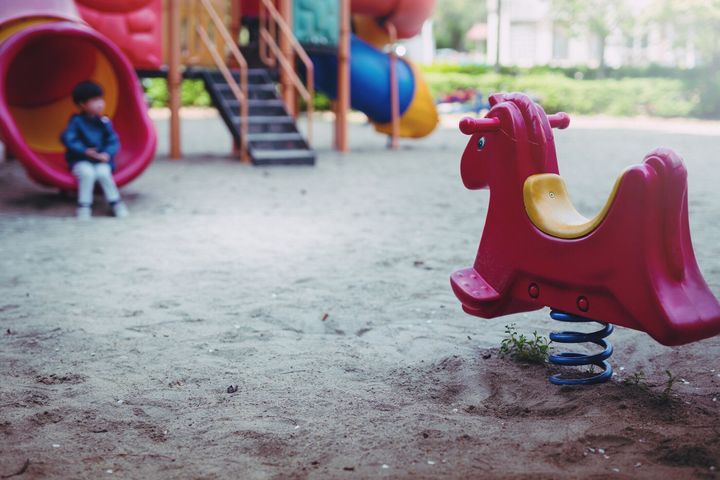小さな男の子は孤独な遊び場で遊んでいます。小さな男の子は、遊び場に不幸な座っています。