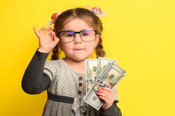 背景にお金と子供たち、大金を持つメガネを持つ金持ちの女の子。