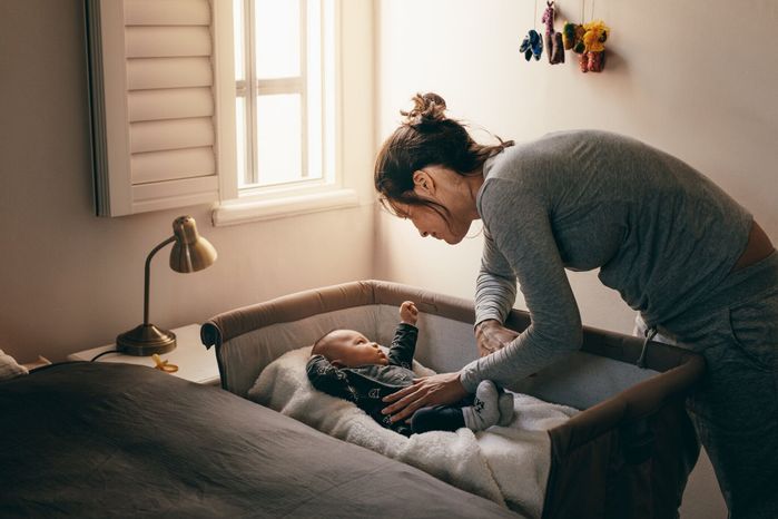 ベビーベッドに寝ている赤ん坊を見て若い母親