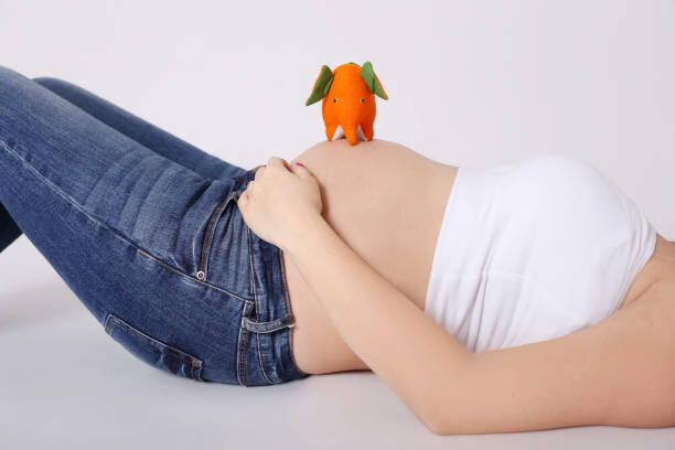 腹にオレンジゾウのおもちゃで横たわっているジーンズの妊婦