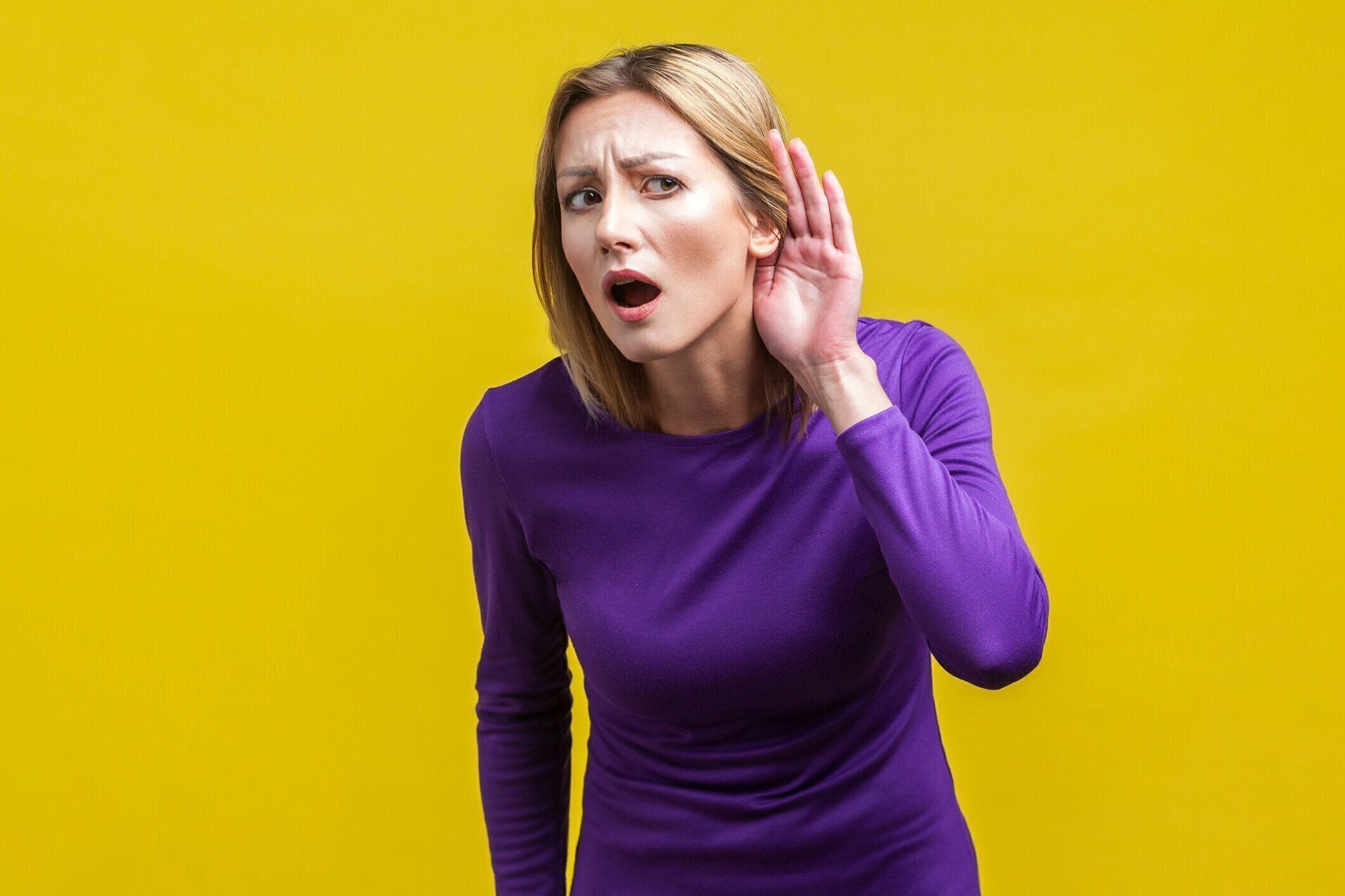 聞こえない!耳の近くに手をつないで好奇心旺盛な女性の肖像画。黄色の背景に隔離された屋内スタジオショット