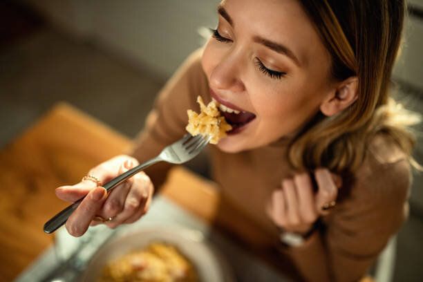 ダイニングテーブルでパスタを食べる若い幸せな女性のクローズアップ。