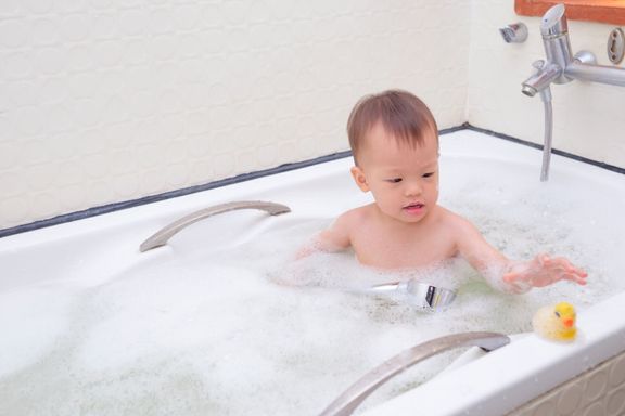 かわいい小さなアジア 18 ヶ月/1 年古い幼児赤ちゃん男の子子供楽しんでバスタブ再生ゴムのアヒルおもちゃに座っています。