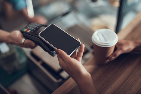 クレジット カード決済機にスマート フォンを置く若い女性の手