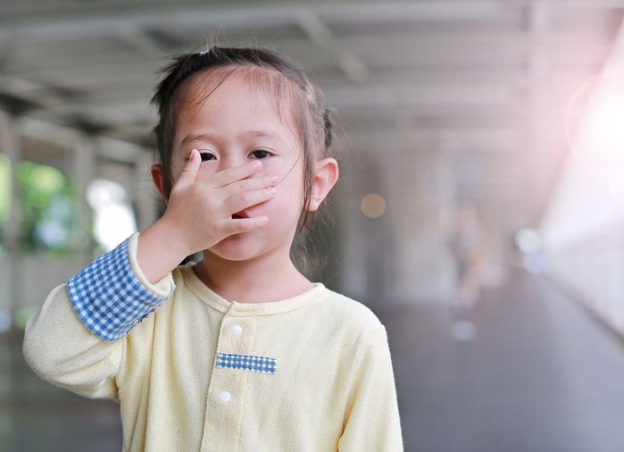 小さなアジアの女の子は彼女の口と彼女の手で鼻を覆います。