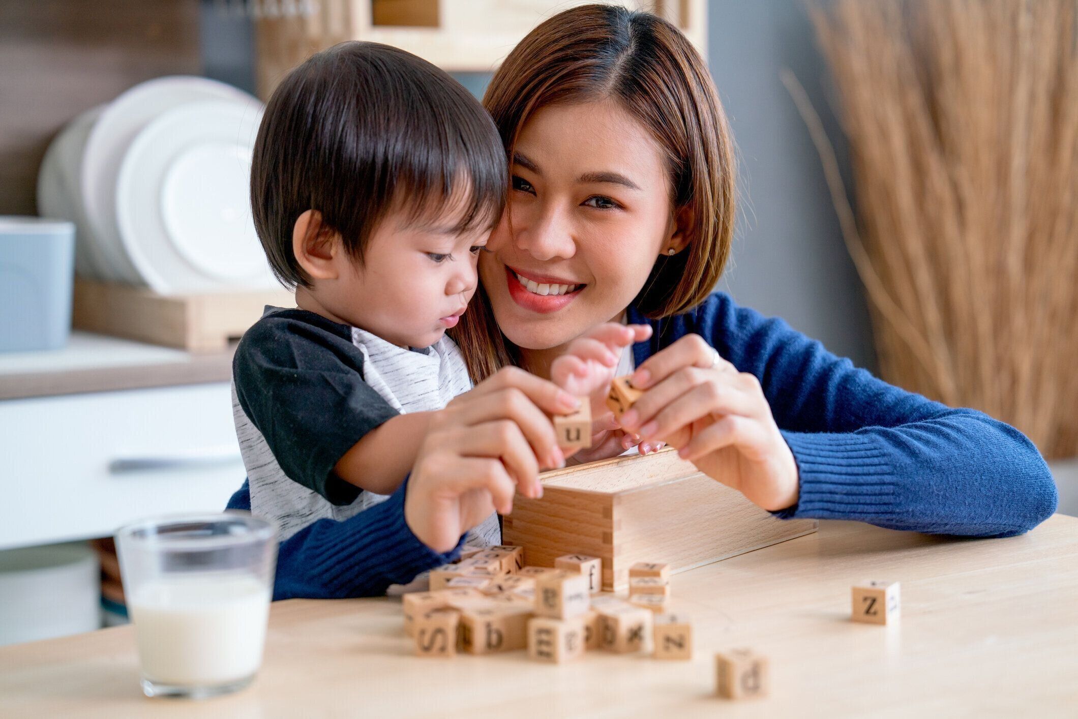 アジアの母親は、彼らの家の台所のエリアで一緒に木製のジグソーパズルをプレイすることを楽しんで、彼らは幸せに見えます。