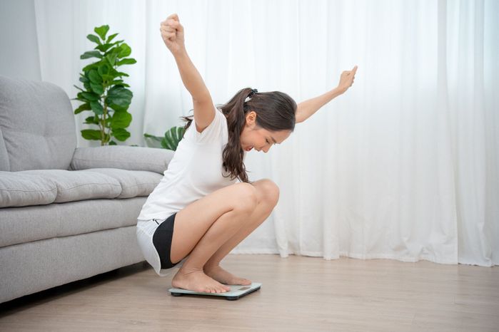 自宅でのウェルネス。ダイエット、ダイエット。幸せそうな顔の表情を持つ体重計の女性。美しいアジア人女性は、栄養士との運動とダイエット計画に参加した後、体重を減らすことに成功�