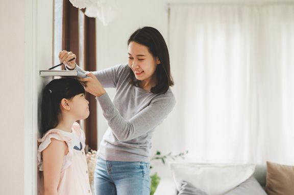 壁の近くの小さな女の子の高さを測定する母親