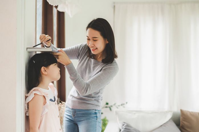 壁の近くの小さな女の子の高さを測定する母親