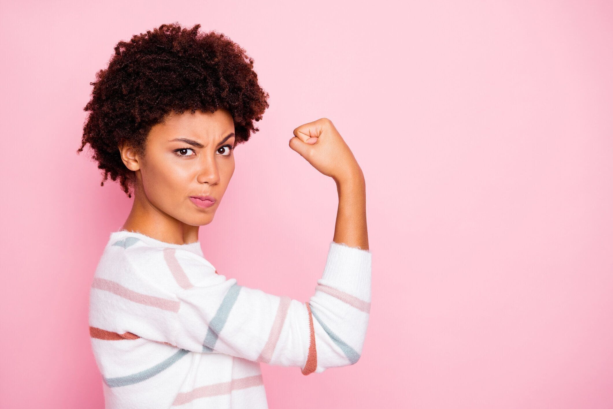 興奮した暗い肌の波状の女性は、ガールフレンドを保護する詐欺師のボーイフレンドに怒って拳を上げる白いストライプのプルオーバー孤立パステルピンクの色の背景を着用