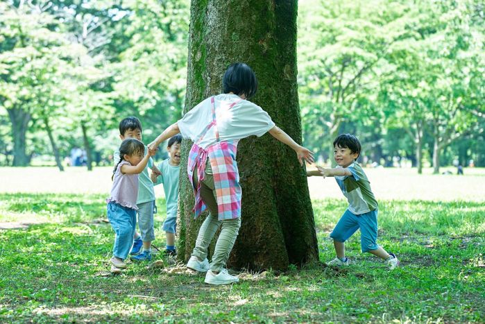 手をつないで木の周りを回る子供と女性