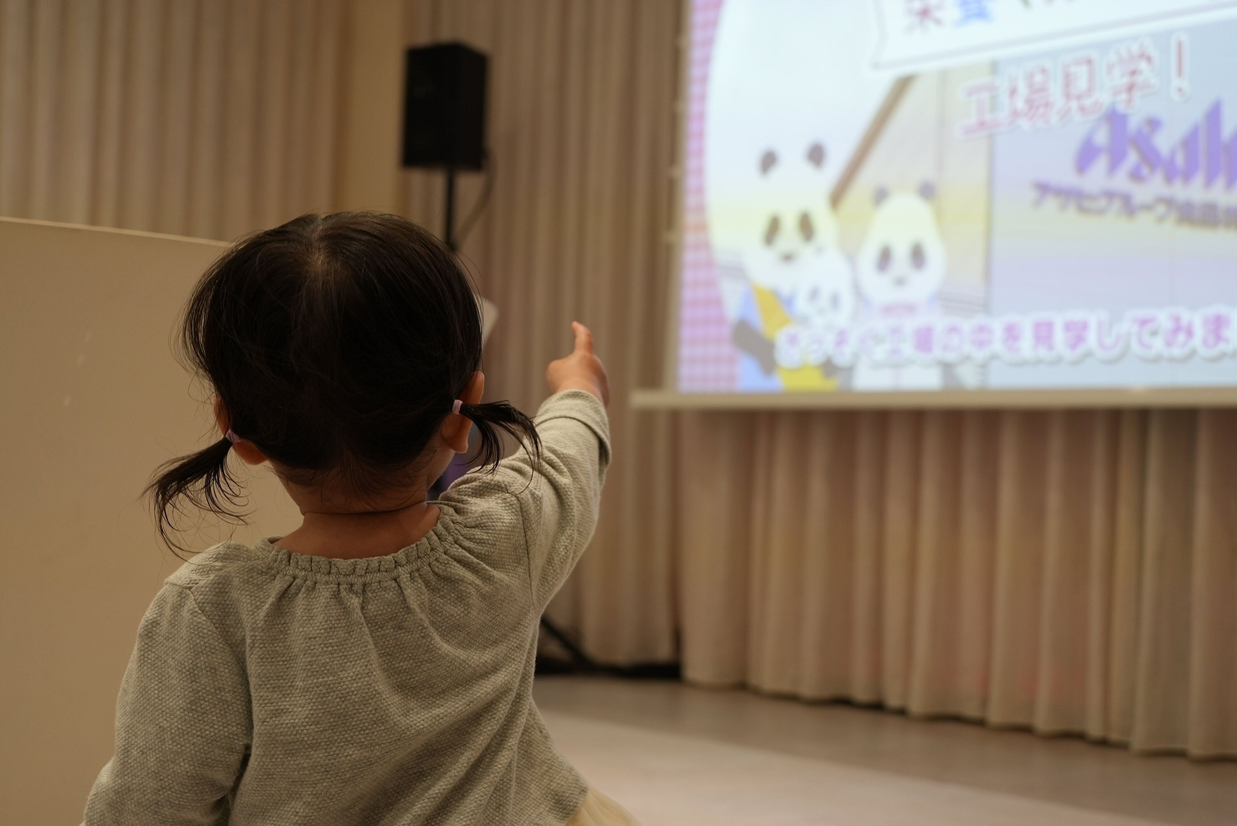 工場見学の映像を指さす赤ちゃん