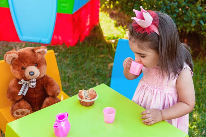 赤ちゃん幼児の女の子がテディベアのテーブルに座っての親友とカップから飲む屋外のティー パーティーで演奏します。