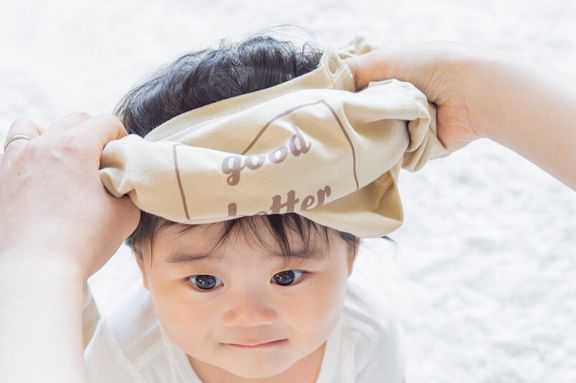 【かぶるタイプの肌着・ウエア お着換えのコツ・2】ウエアをドーナツ状にしてから、赤ちゃんの頭を通す