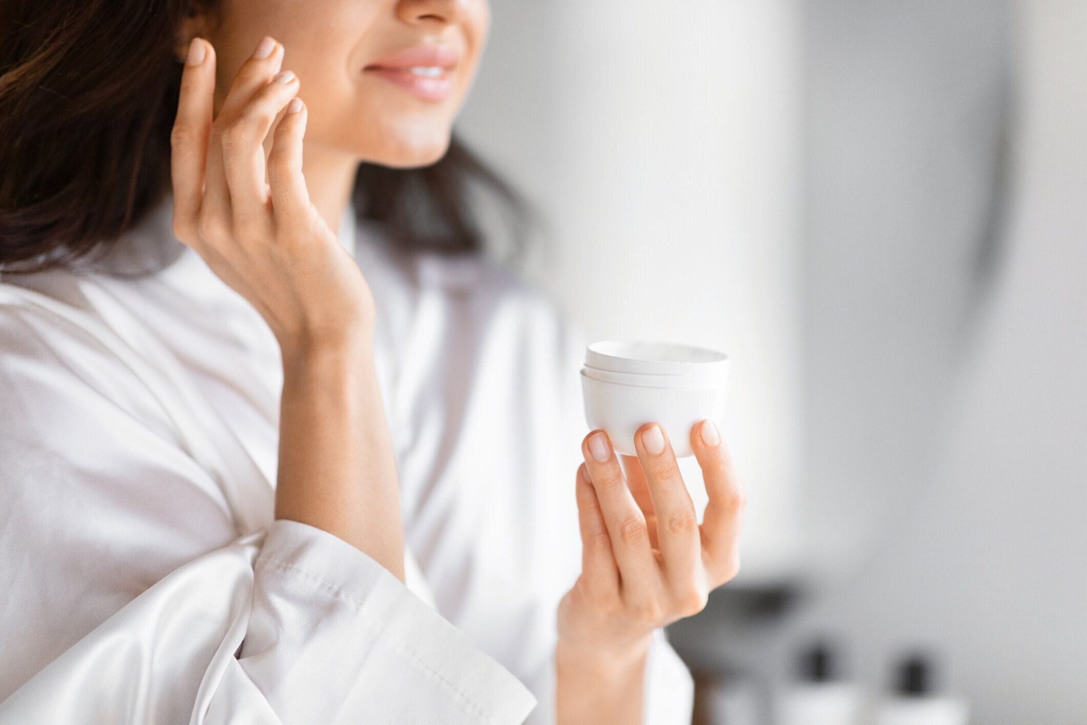 スキンケアクリームの瓶を持つ女性