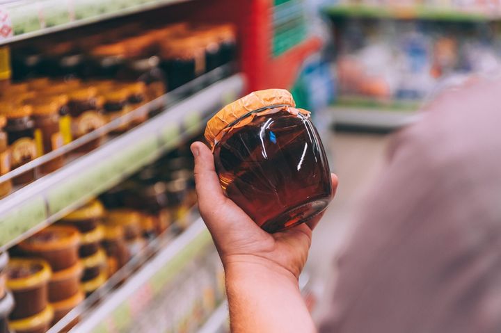 スーパーの男は蜂蜜のガラス瓶を持っています。