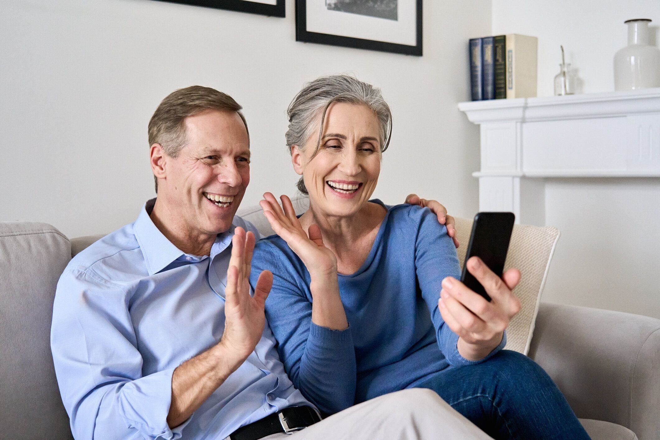 携帯電話でオンラインビデオ通話をする手を振る幸せな老夫婦。成熟した引退した50年代の祖父母は、仮想会議のビデオ通話チャットを楽しんだり、話したり、自宅のソファに座っているス�