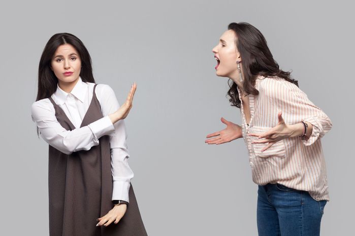 カメラを見て、彼女に叫んで別の女の子に停止または無視を示す若い女の子の肖像.2人の友人やパートナーとの対立。