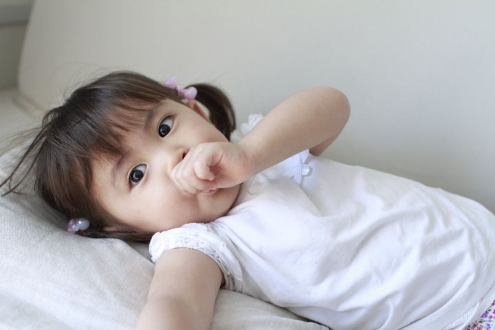 (2 歳) 彼女の指をしゃぶりで日本人の女の子を横になっています。