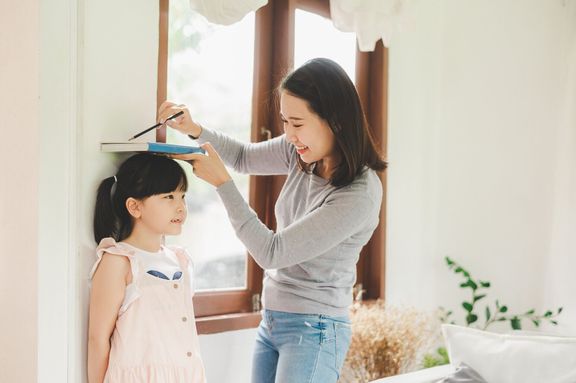 壁の近くの小さな女の子の高さを測定する母親