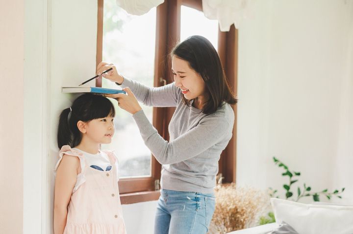 壁の近くの小さな女の子の高さを測定する母親