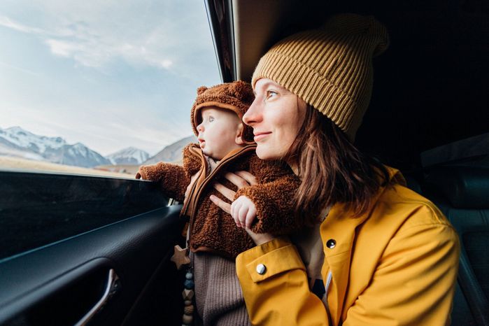 笑顔の若くて美しい女性の母親と驚いた顔をした赤ちゃんが車の窓から山を見る