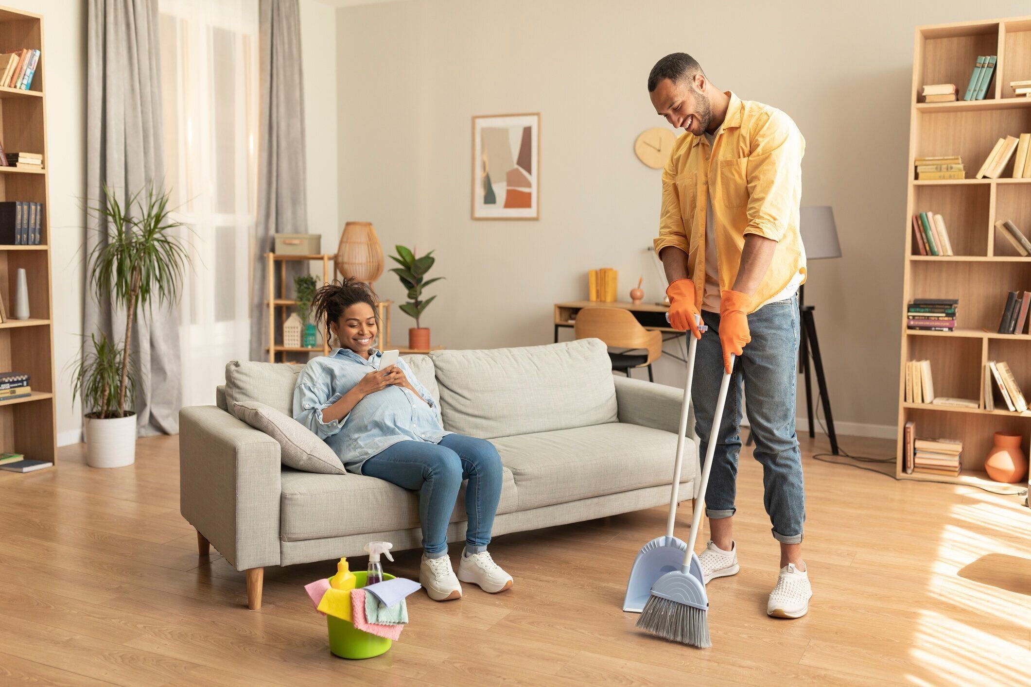 妊娠と家事手伝い。妊娠中の妻が休んでソファに座っている間に家を掃除する黒人夫