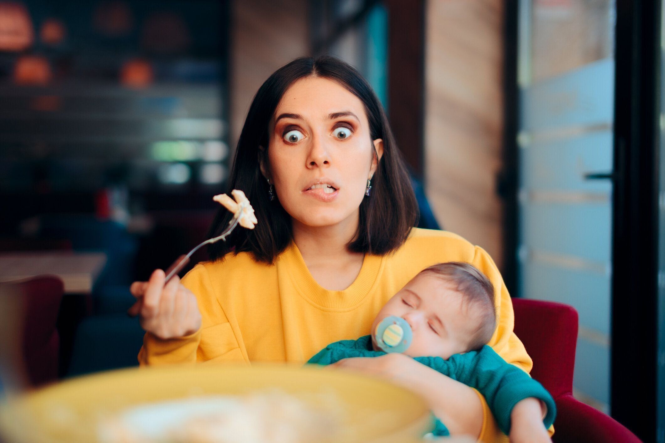 テーブルで眠っている赤ちゃんを抱いて食べるママ